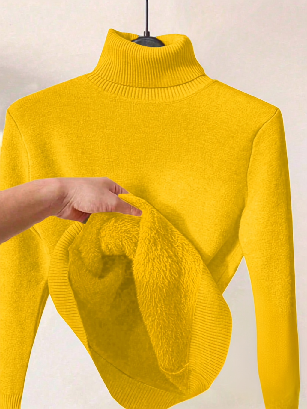 A bright yellow ribbed turtleneck sweater displayed on a hanger, with a hand pulling down the front to show a plush, fuzzy inner lining.