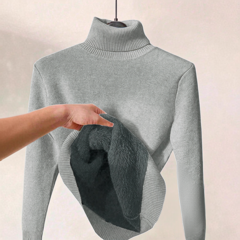 A light gray ribbed turtleneck sweater displayed on a hanger, with a hand lifting the hem to show a dark plush fleece lining.