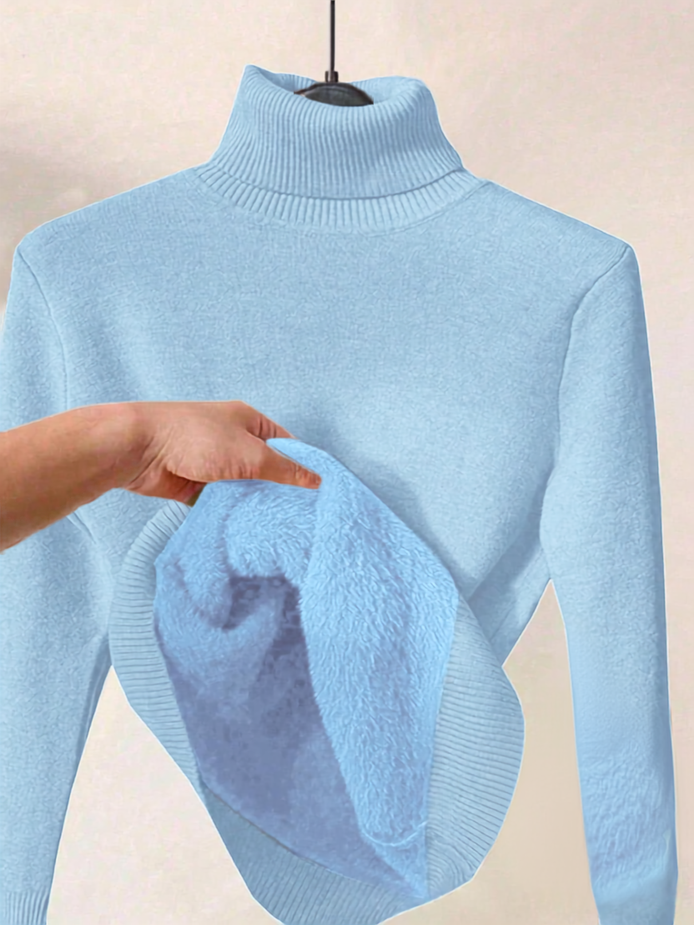 A light blue ribbed turtleneck sweater displayed on a hanger, with a hand holding up the soft plush lining of the collar.