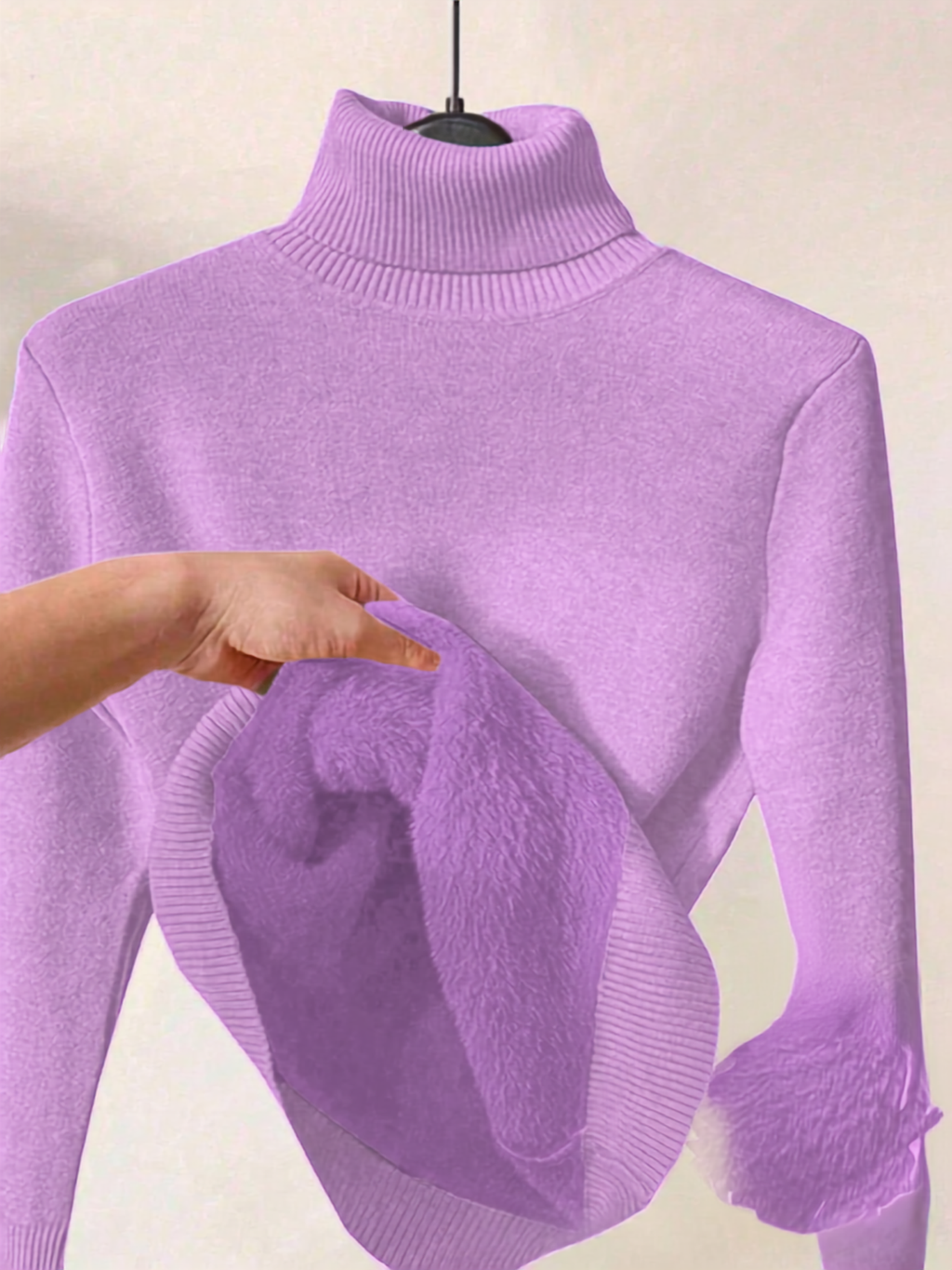 A lavender purple ribbed turtleneck sweater displayed on a hanger, with a hand pulling out the soft fuzzy inner lining of the collar.